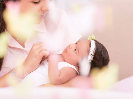 Cute young mother looking on sweet newborn daughter, take care about her, photo with soft focus, happy motherhood conceptの写真素材