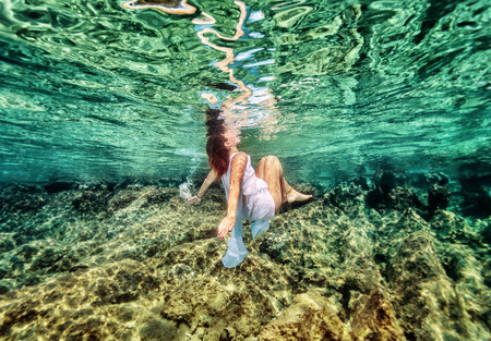 Dancing underwater, beautiful young female swimming in the sea near beautiful coral garden, active lifestyle, summer holidays and vacation conceptの写真素材