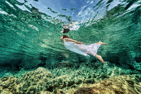 Swimming in transparent sea, emerges from clear sea, wearing fashionable white dress, luxury summer vacation, freedom and enjoyment conceptの写真素材