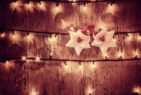 Photo of abstract Christmas glowing background, yellow electrical garland on old wooden door, shiny decorations on dark grunge wall, two Santa Claus stars, New Year festive ornamentの写真素材
