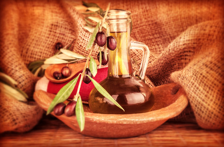 Extra virgin olive oil in the bottle decorated with fresh ripe olive branch on burlap background, beautiful food still life, healthy eating conceptの写真素材