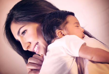 Closeup portrait of cute little baby sleeping on mothers shoulder, happy young loving family, new life conceptの写真素材