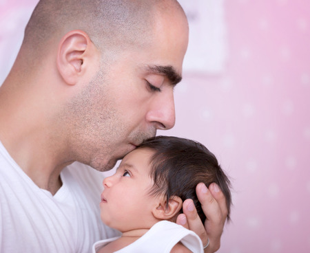 Closeup portrait of a daddy and his baby girl at home, with gentleness kissing his cute newborn...
