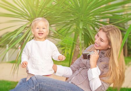 Cheerful mother taking picture of her cute little daughter in the park, happy young family having fun outdoors, parental love and enjoymentの写真素材