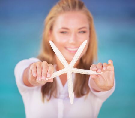 Soft focus portrait of beautiful blond female holding in hands starfish, having fun on the beach, beauty of underwater natureの写真素材