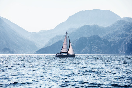 Beautiful sea landscape, sailboat sailing on the distance on great majestic mountains background,...