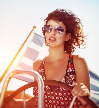 Beautiful woman driving sailboat, steering wheel in mild yellow sunset light, enjoying water travel in the evening, active summer vacationの写真素材