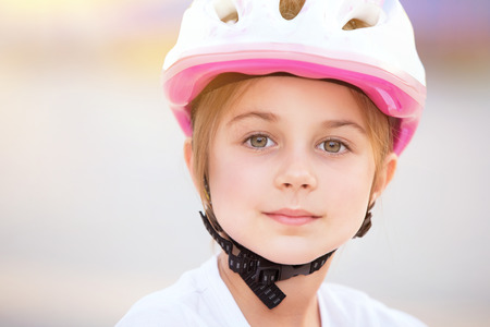 Closeup portrait of cute little biker girl wearing pretty pink and white helmet, having fun outdoors, with pleasure spending time in summer campの写真素材