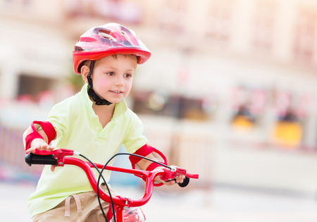 Little boy playing outdoors, cute cheerful child having fun in summer camp, nice kid riding on red stylish bicycle on blur urban background, enjoying carefree summer holidaysの写真素材