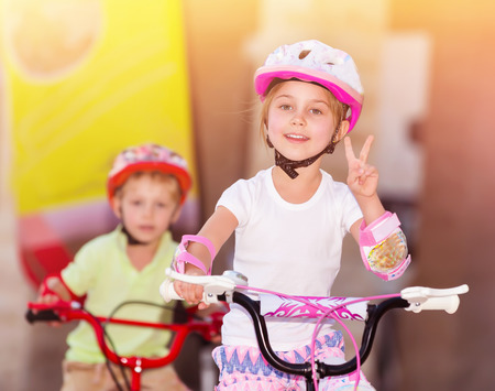 Happy children racing on bicycles, brother and sister organized sports competition, siblings with pleasure playing together, winner girl hand shows the sign of peaceの写真素材