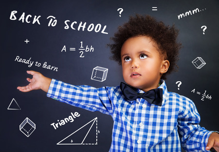Portrait of smart curly African American schoolboy in the school on mathematics lesson, solving task...