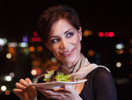 Pretty woman having dinner at night in outdoors restaurant, eating fresh green salad, healthy...