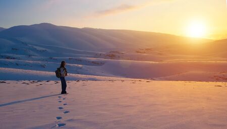 Traveler woman in the mountains enjoying beautiful sunset view, active winter holidays, amazing...