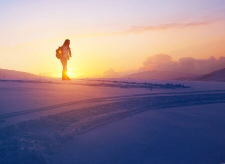 Woman enjoying beautiful sunset view from the high snowy mountain, discovering wild nature, active winter holidaysの写真素材