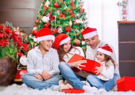Portrait of happy young parents with their two precious kids are considered gifts, sitting on the floor near festive Christmas treeの写真素材