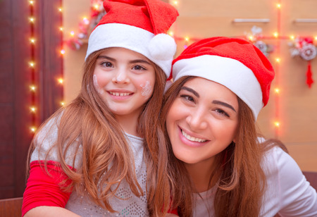Closeup portrait of mother with cute little daughter wearing Santa hat baking on the kitchen at home, enjoying traditional Christmas preparationの写真素材