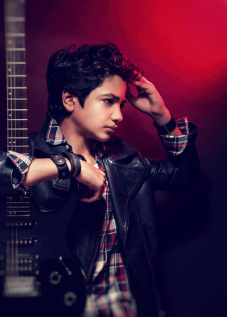Portrait of attractive teen model posing with guitar in the studio over red background, beautiful...