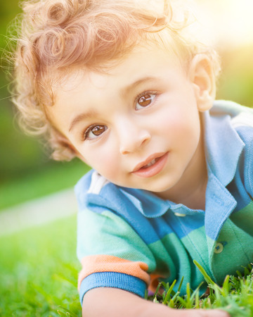 Closeup portrait of a cute little baby boy lying down on the grass, having fun in the park, spending summer holidays outdoorsの写真素材