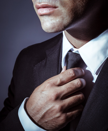 Closeup photo of a serious businessman wearing stylish black suit and tie over dark background, face part, mens wear fashion conceptの写真素材