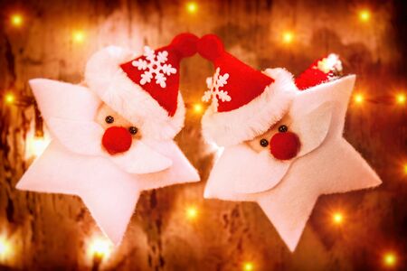 Beautiful Christmas decoration, two Santa Claus toys in a stars shape decorating glowing wooden wall, festive still lifeの写真素材