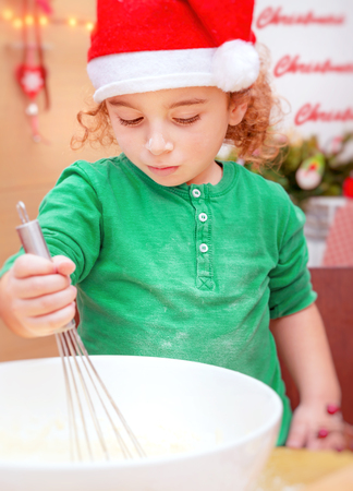 Portrait of a cute little boy wearing red Santa hat making Christmas cookies at home, happy festive time, preparation for winter holidaysの写真素材