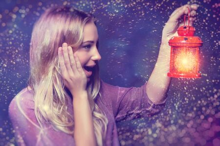 Portrait of a beautiful excited woman surprised looking on a glowing light in lantern, true miracle in Christmas eve, happy magical nightの写真素材