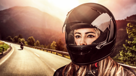 Closeup portrait of a beautiful woman wearing helmet, biker on the mountainous road in mild sunset...