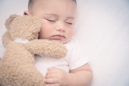Cute little baby in the bed, adorable infant sleeping with little bear, nice little boy in the morning, healthy childhood, peace and relaxation conceptの写真素材