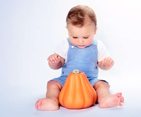 Cute little baby boy sitting in the studio over clean background and with wonder looking on the orange pumpkin, happy Thanksgiving day, traditional American autumn family holidayの写真素材