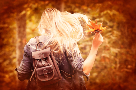 Vintage style photo of a joyful blond girl runing in autumn forest, holding in hand dry tree leaves, having fun in autumn parkの写真素材