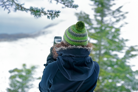 Woman photographing nature by her smartphone, traveler girl taking picture of the mountains covered...