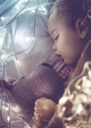 Cute little baby sleeping at home in his bed with his best friend, soft toy dog, vintage style photo with glowing lights, childhood dreams
の写真素材