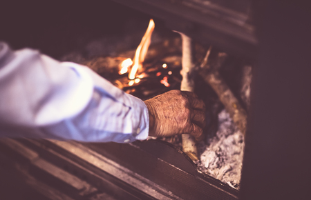 Man kindle a fire in the fireplace, grandpa making warmth and cozy atmosphere in the country house, romantic and peaceful winter evening
の写真素材