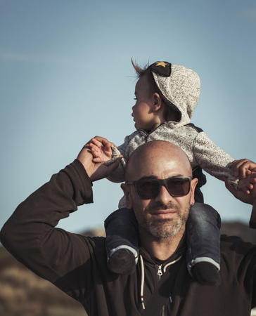 Child is sitting on his father's shoulders, handsome dad playing with his cute little son, enjoying parenthood, family love conceptの写真素材