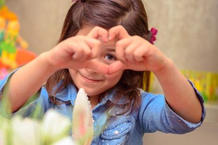 Portrait of a cute little girl making heart, sweet precious child showing love, enjoying traditional...