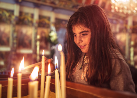 Little girl in the church on Easter, puts a candle and prays to God, enjoying happy religious holiday, good peaceful atmosphere in the holy placeの写真素材