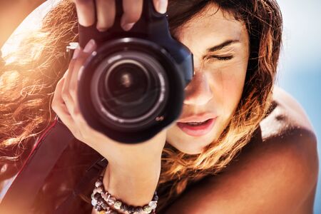 Closeup portrait of a beautiful girl with camera on the beach, cute young photographer taking picture, creative hobby, happy active summer vacationの写真素材