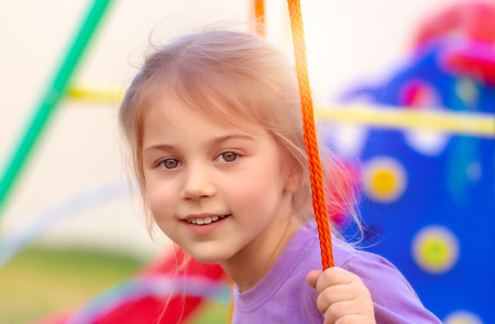 Closeup portrait of a cute little girl on the swing on playground, happy child with pleasure spending time in the yard, enjoying spring holidaysの写真素材