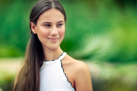 Portrait of a beautiful girl on blurry green natural background, nice attractive female without makeup, genuine beauty of young womanの写真素材