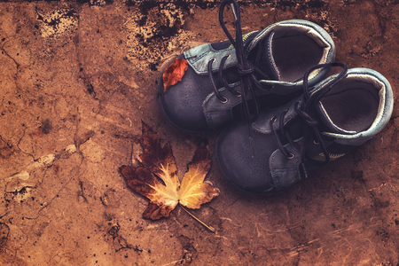 Little baby shoes on the ground outdoors, autumnal boots with dry tree leaves on it, warm seasonal clothes for kidsの写真素材