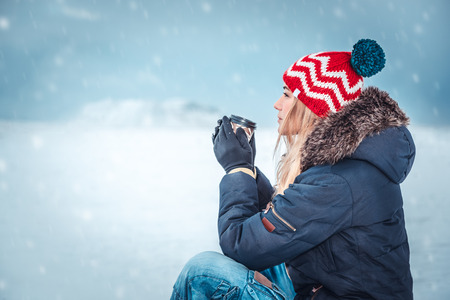 Nice girl sitting outside on a snowy winter day and having coffee, enjoying peaceful wintertime vacationの写真素材