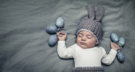 Portrait of an adorable newborn child dressed in a knitted costume of an Easter bunny with stylish colored eggs, copy space, Easter ideas for kidsの写真素材