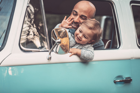 Happy family in the car, summer travel in the van, cheerful father with his adorable little son driving wagon, smiling and waving his hands, enjoying parenthoodの写真素材