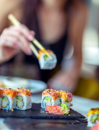 Eating sushi in the restaurant, a woman using chopsticks takes a piece of roll, enjoying tasty and healthy food, traditional Asian cuisineの写真素材