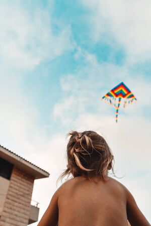 Happy child launches a kite, baby looking up at a multi-colored kite soaring in the sky, happy childhood, kid enjoying summer holidays, photo with copy space, freedom conceptの写真素材