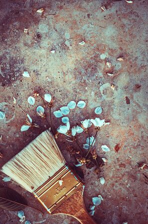 Closeup photo of a paint brush decorated with petals of a blooming flowers, gray grunge stone table background, stylish still life, photo with copy space, decor and art crafts ideasの写真素材
