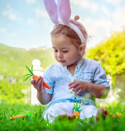 Portrait of a cute little baby boy dressed as an Easter bunny, adorable kid playing with carrots and...