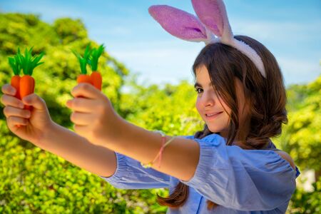 Portrait of a sweet little girl dressed as bunny playing with carrotsの写真素材