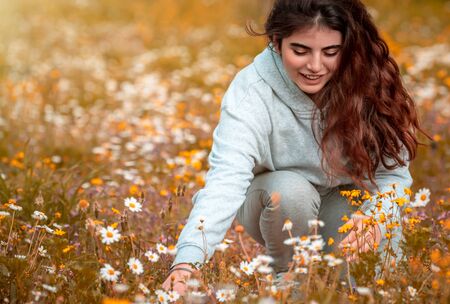 Teenager enjoying springtime holidays in the countryside, happy nice girl with pleasure picking little daisy flowers, spending quality time outdoors, breathing fresh airの写真素材