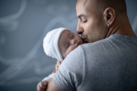 Portrait of a happy father with gentleness kissing his newborn baby, young family with pleasure spending time at home, love conceptの写真素材